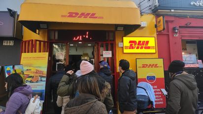 Personas forman una fila para entrar al DHL que está ubicado frente a la Embajada de Venezuela.