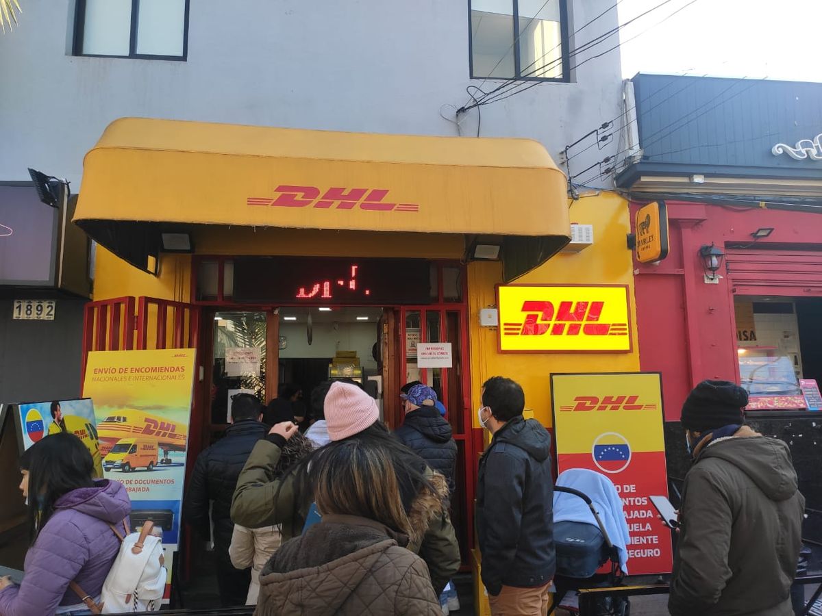 Personas forman una fila para entrar al DHL que está ubicado frente a la Embajada de Venezuela.