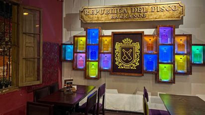 Los locales de República del Pisco se distinguen por sus comidas, tragos y rasgos decorativos como su botellero multicolor.